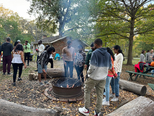 students cooking hot dogs over fire