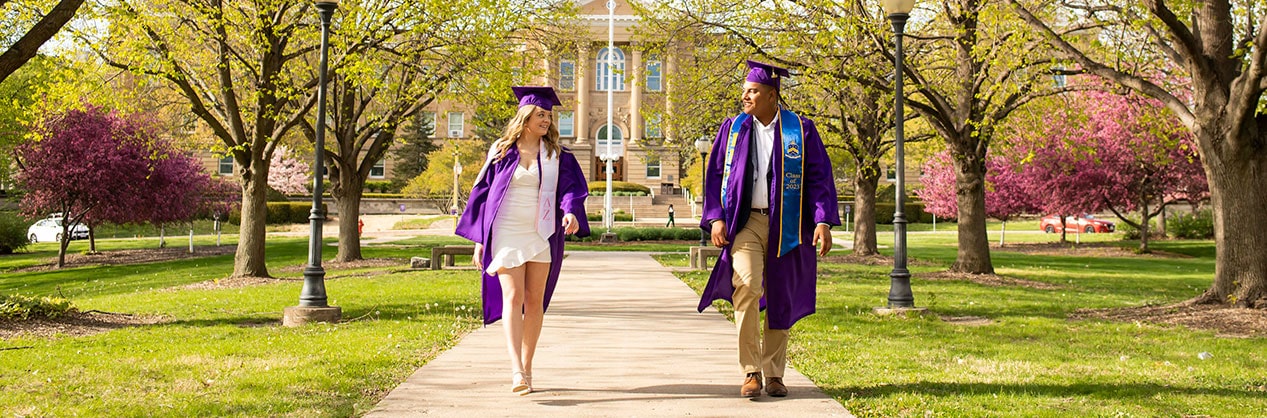 students in graduation caps and gowns walking in front of Sherman Hall