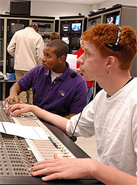Two broadcasting students gain hands-on experience at control board. Students working at sound board.