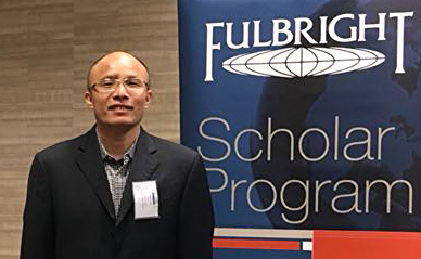 Fanbin wearing a black blazer, standing in front of a Fulbright Scholar Program sign