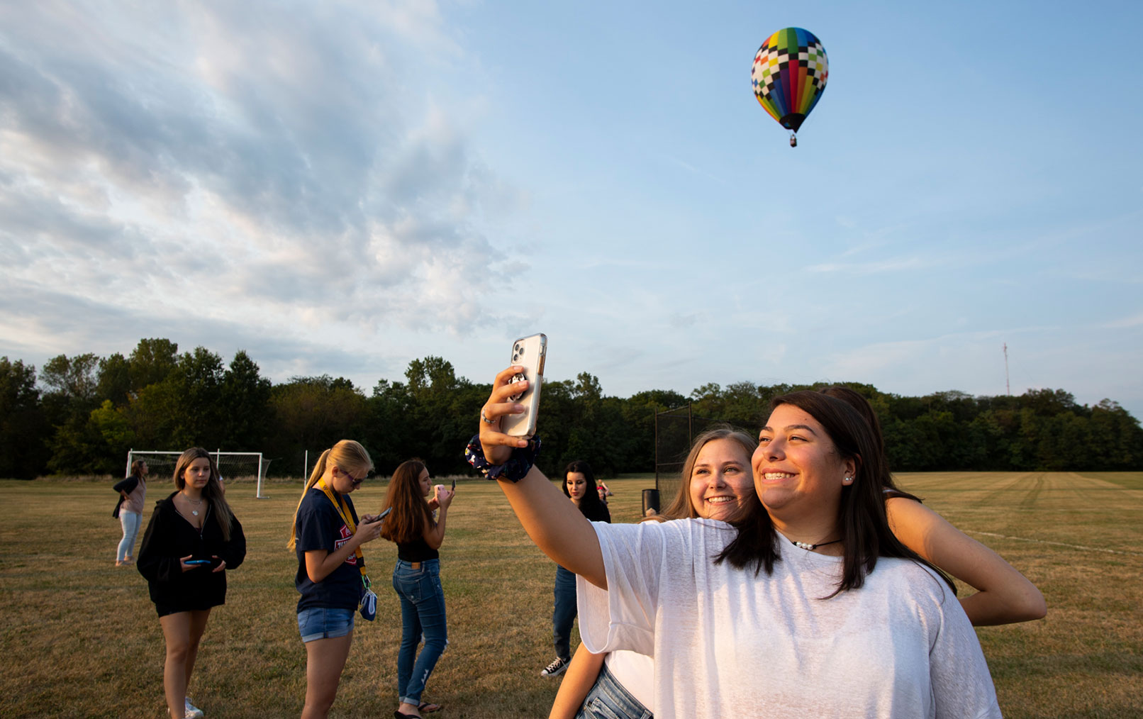 college students taking photos in a field with a hot air balloon in the sky