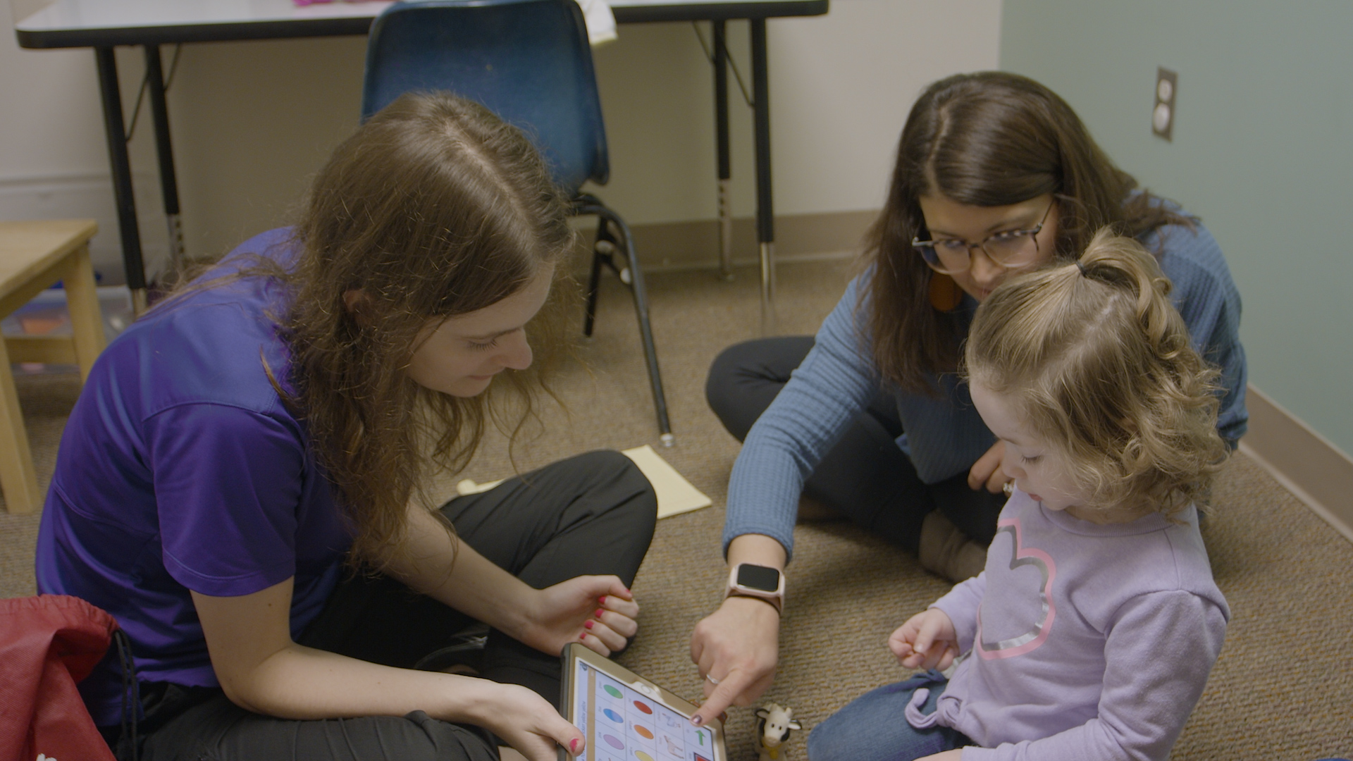 two therapists working with child on iPad