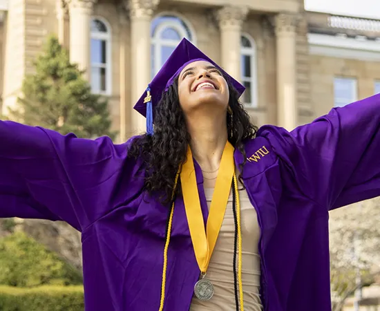 student in purple graduation gown looking up at the sky and smiling