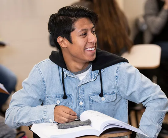 a student sitting at a classroom desk looking to the side and smiling