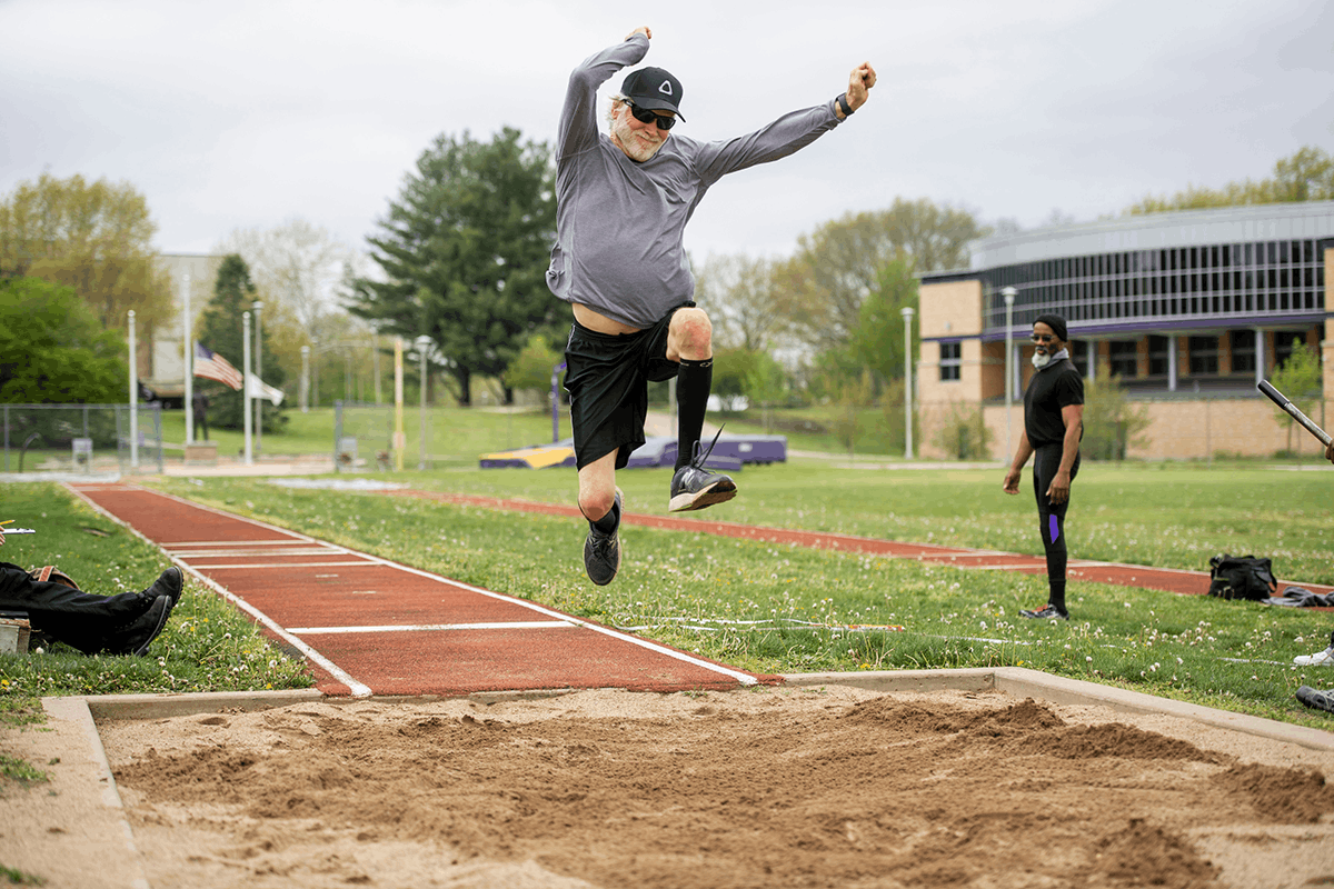 A senor person in mid-air performing a long jump on a track field.