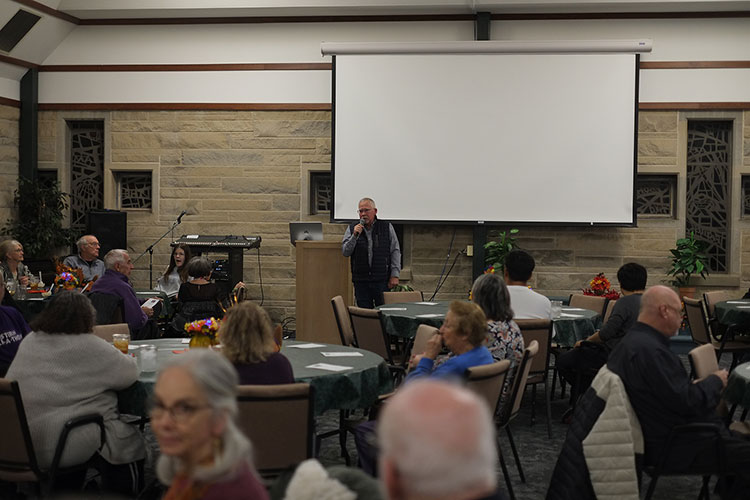 a man speaking to the group of people at tables