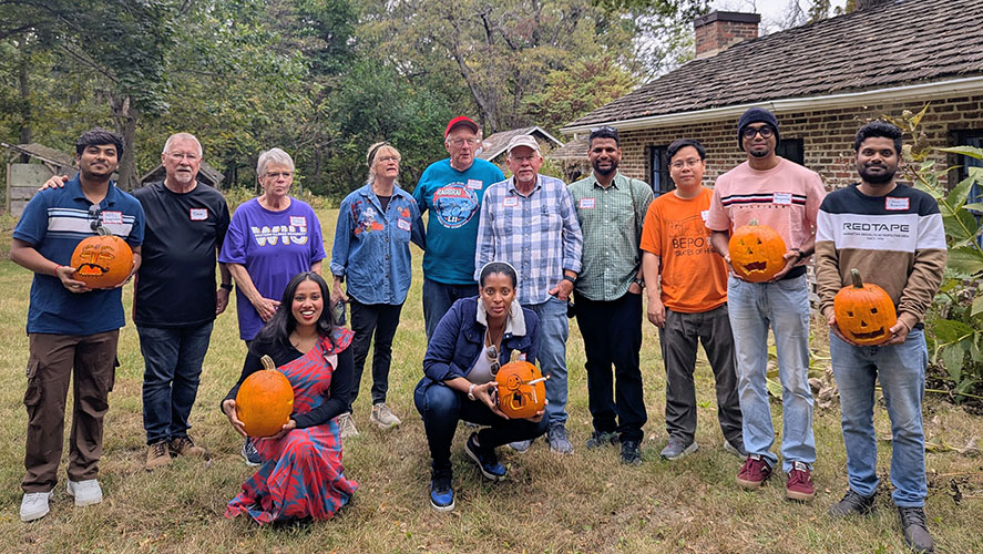 a group of international students holding carved pumpkins with a few local volunteers