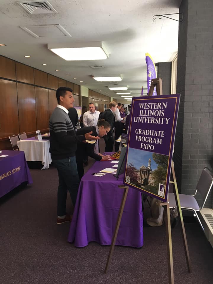 Students speaking with graduate program representatives at individual tables.