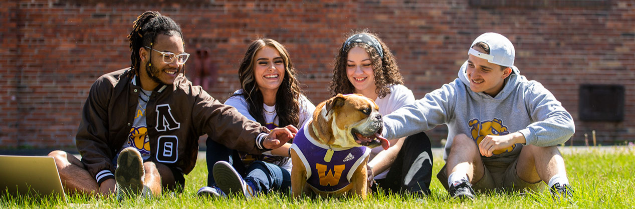 students sitting in the grass, petting Colonel Rock, the bulldog live mascot