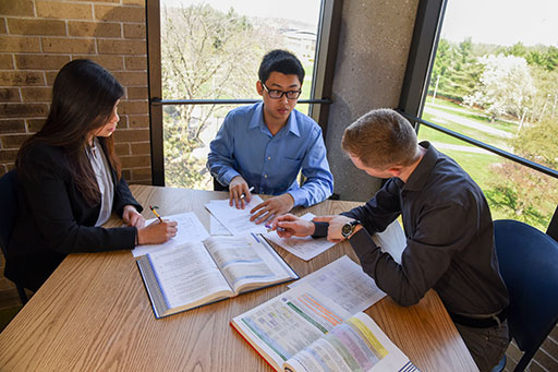 Three students at a table studying academic books and notes