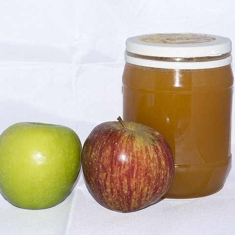 Two apples beside a jar of honey