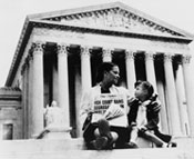 Photo of a woman and a small girl sitting on the steps of a court house holding a newspaper that reads High Court Bans Segregation In Public Schools.