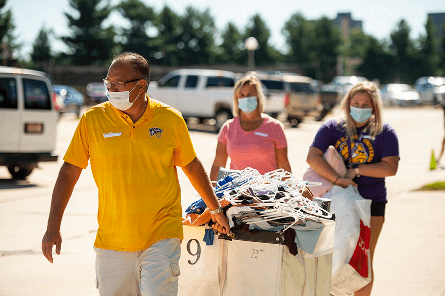 Photo of man pulling cart with students stuff in it during move in and rest of family following