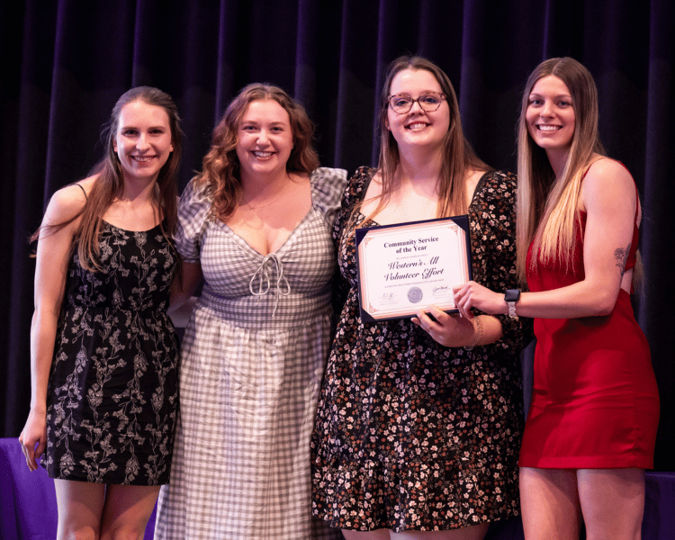 4 individuals holding an award on a stage.
