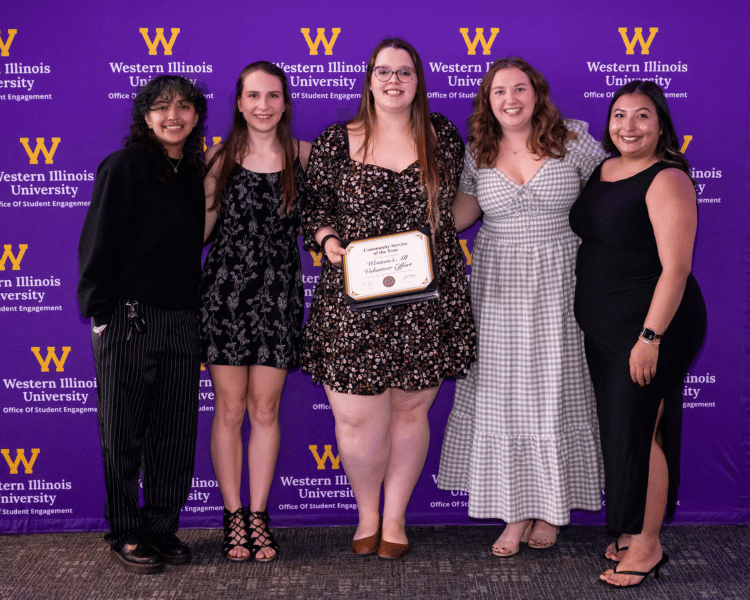 5 individuals holding an awards against a WIU prurple background. 