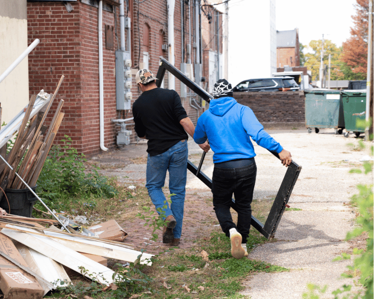 2 individuals holding building scraps taking it to a garbage.