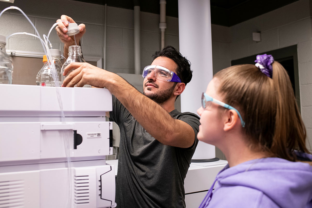 two students working with lab equipment while wearing safety goggles