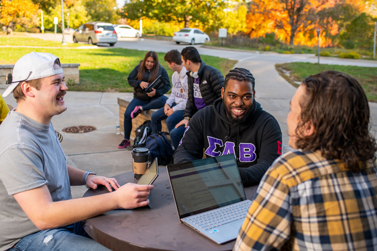 group of students sitting at a table outside talking and laughing together